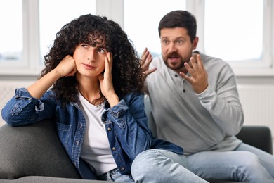 Emotional couple having quarrel on sofa at home, selective focus. Relationship problems