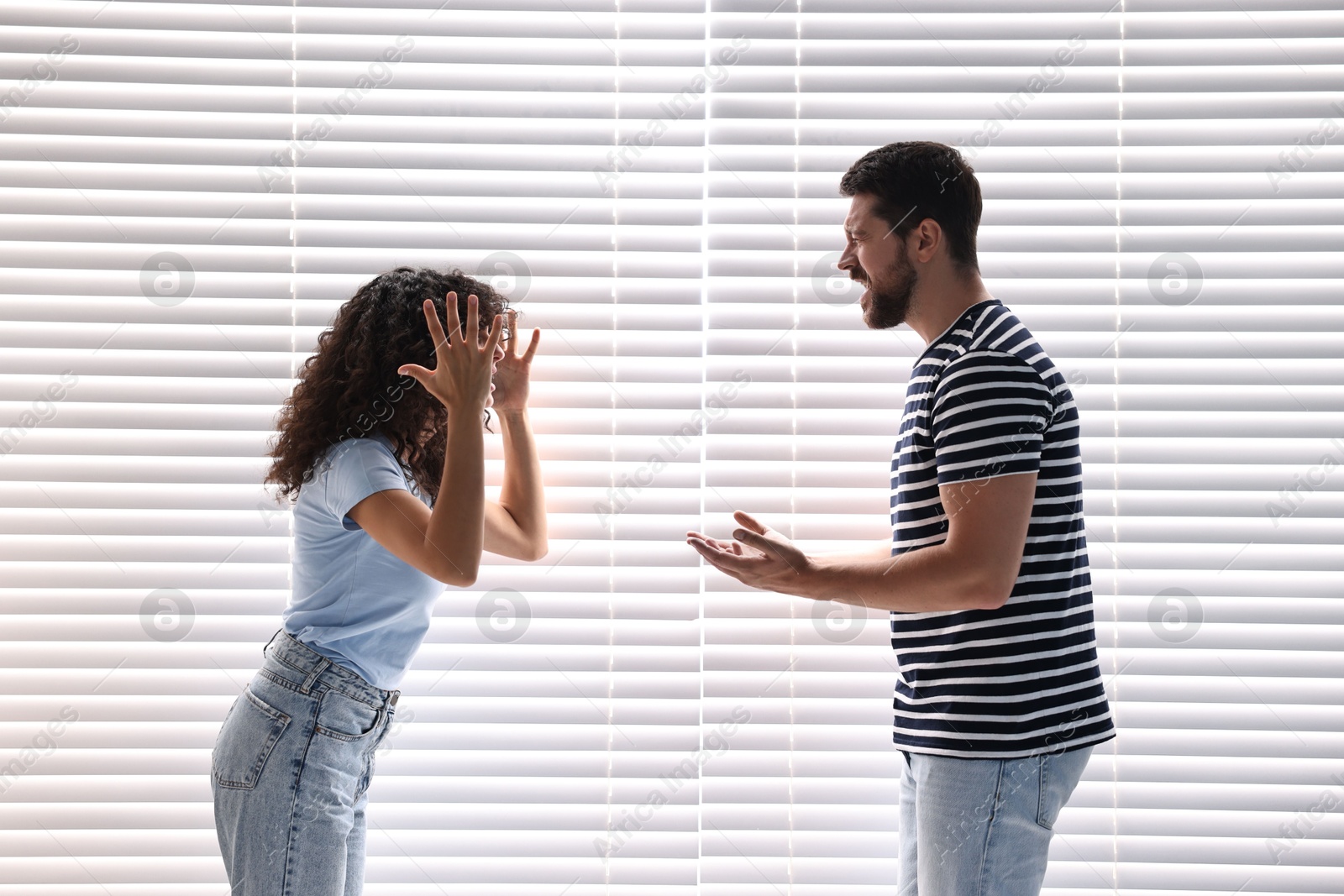 Photo of Emotional couple arguing against white blinds. Relationship problems