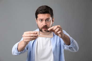 Photo of Emotional man taking his lost hair from comb on gray background. Alopecia problem