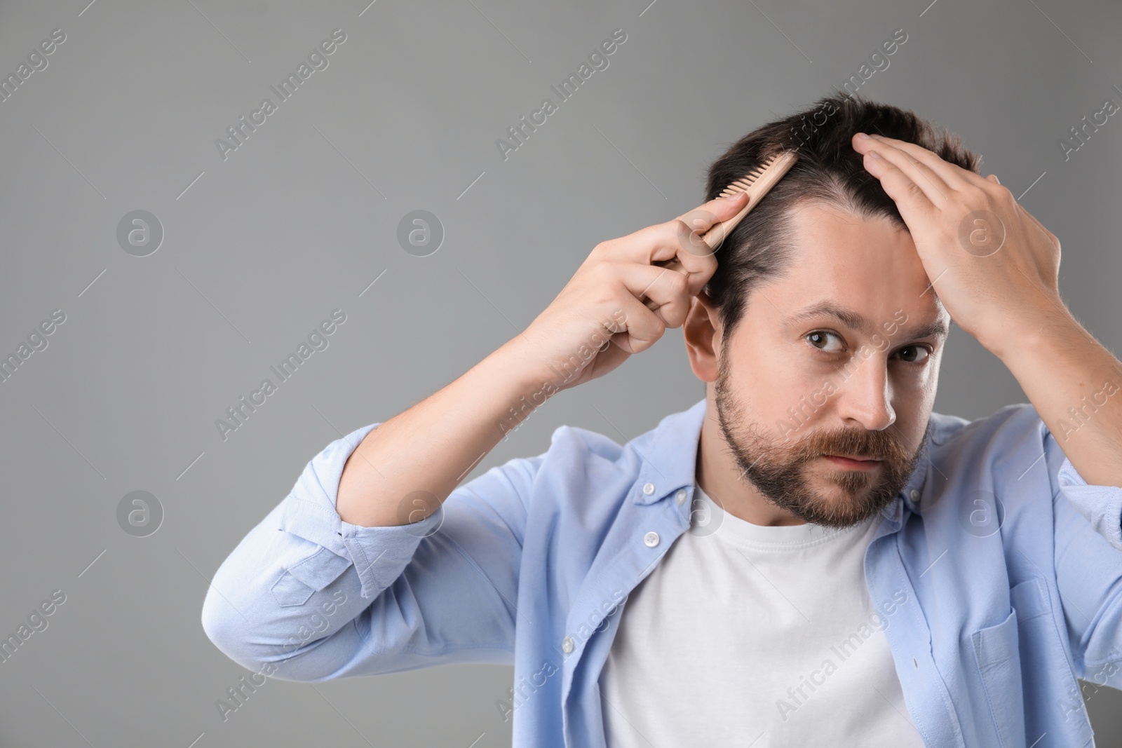 Photo of Man brushing his hair on gray background, space for text. Alopecia problem