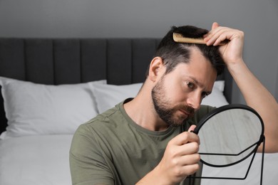 Photo of Man brushing his hair near mirror indoors. Alopecia problem