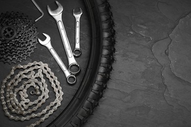 Parts of bicycle and tools on black table, flat lay. Space for text