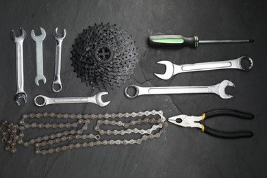 Parts of bicycle and tools on black table, flat lay