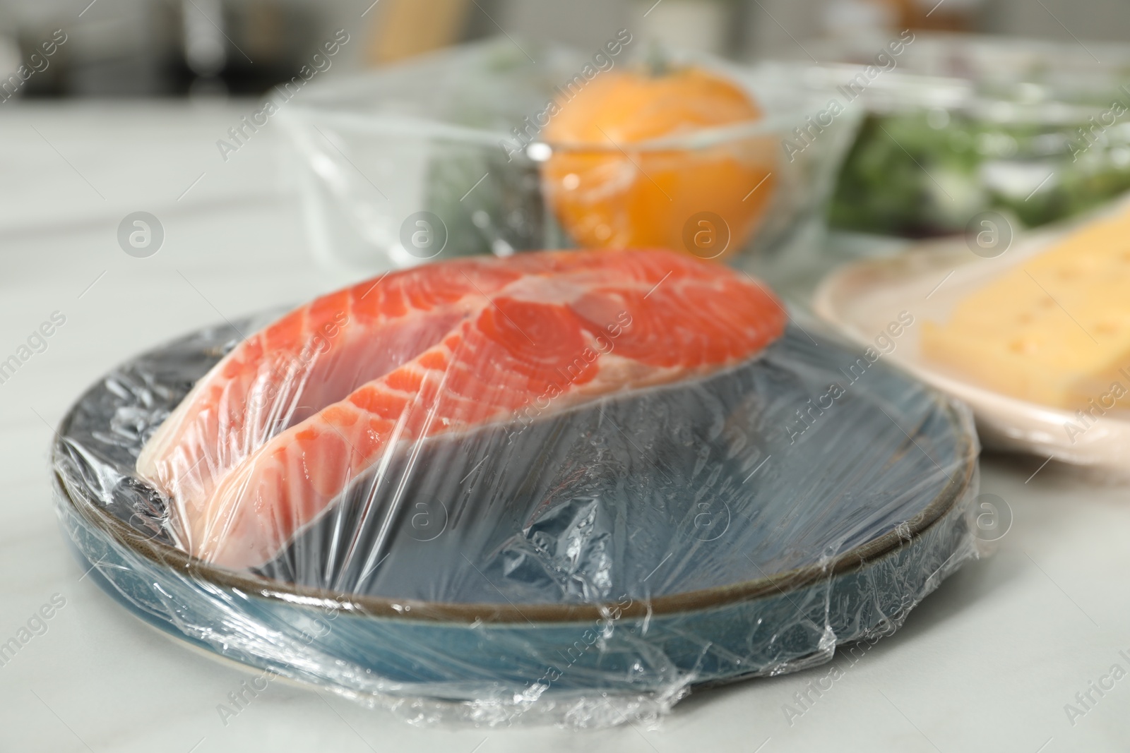 Photo of Plate of salmon with plastic food wrap on white table, closeup