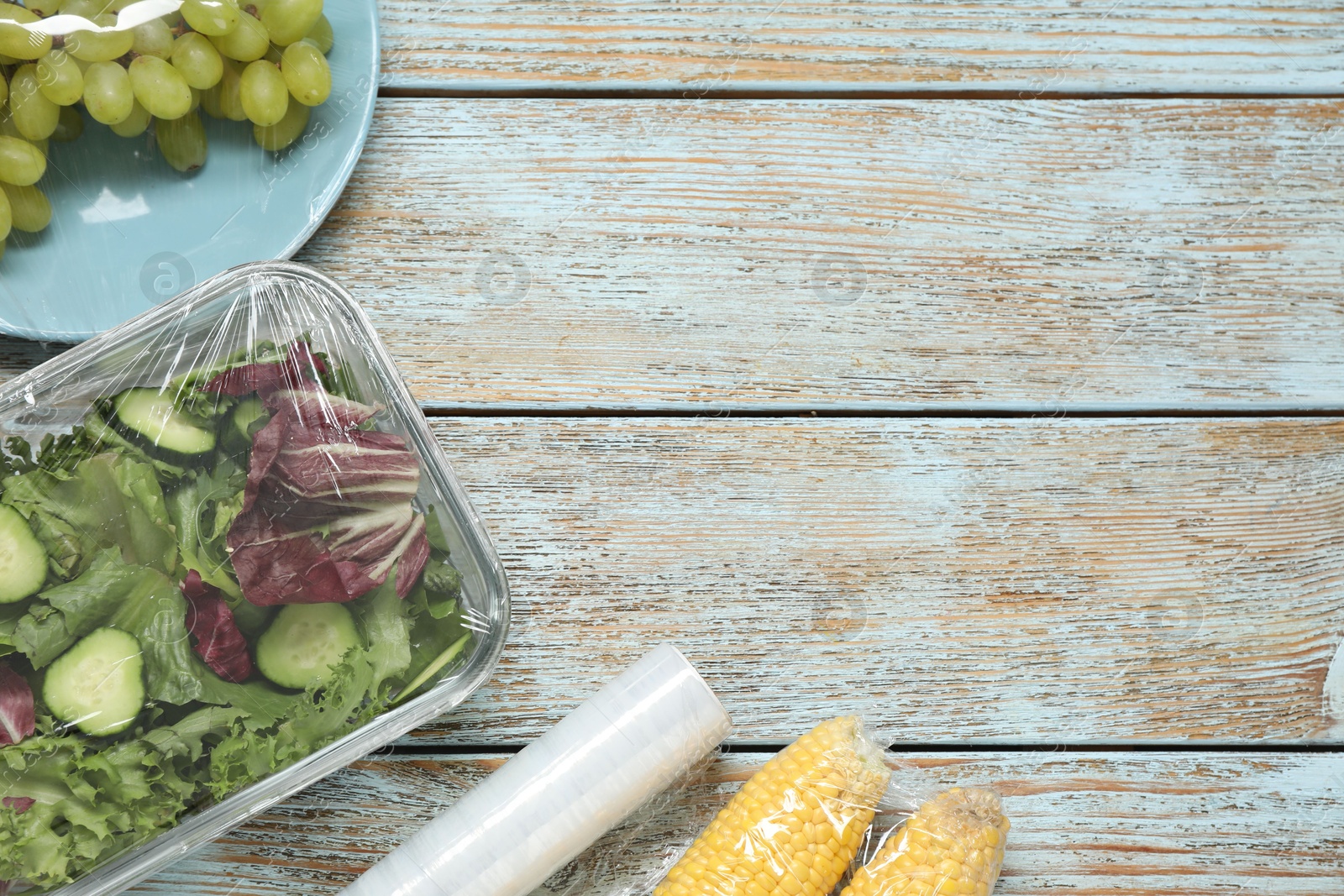 Photo of Different products with plastic food wrap on wooden table, flat lay. Space for text