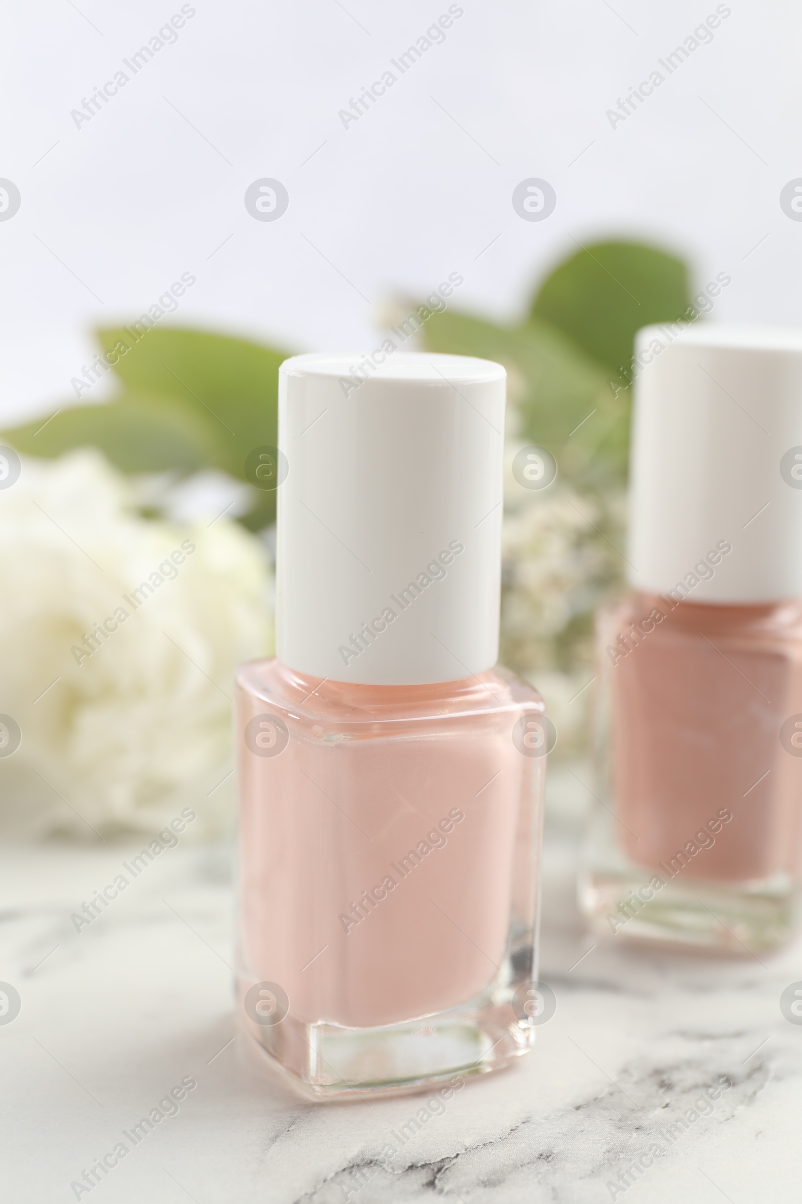 Photo of Nail polishes in bottles on white marble table, closeup