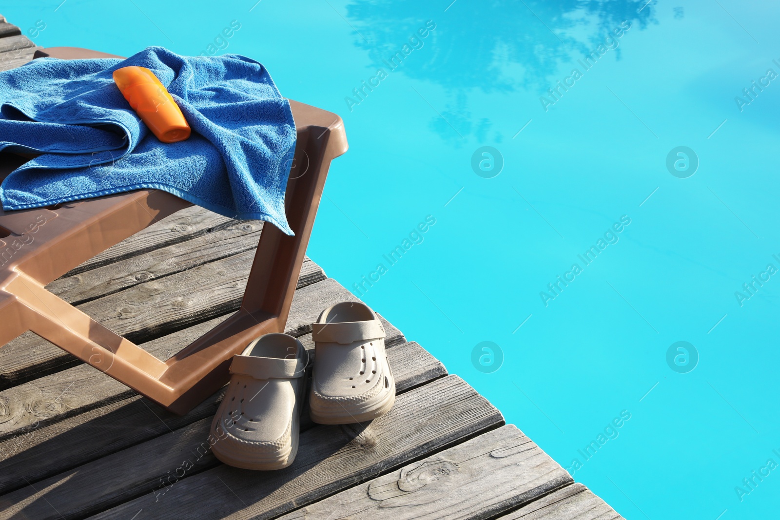 Photo of Beach accessories and sun lounger on wooden deck near outdoor swimming pool