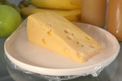 Plate of cheese with plastic food wrap on shelf in refrigerator, closeup