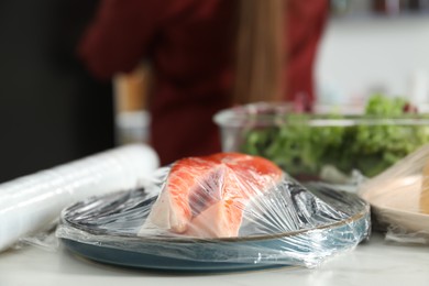 Photo of Plate of salmon with plastic food wrap on white table in kitchen, closeup