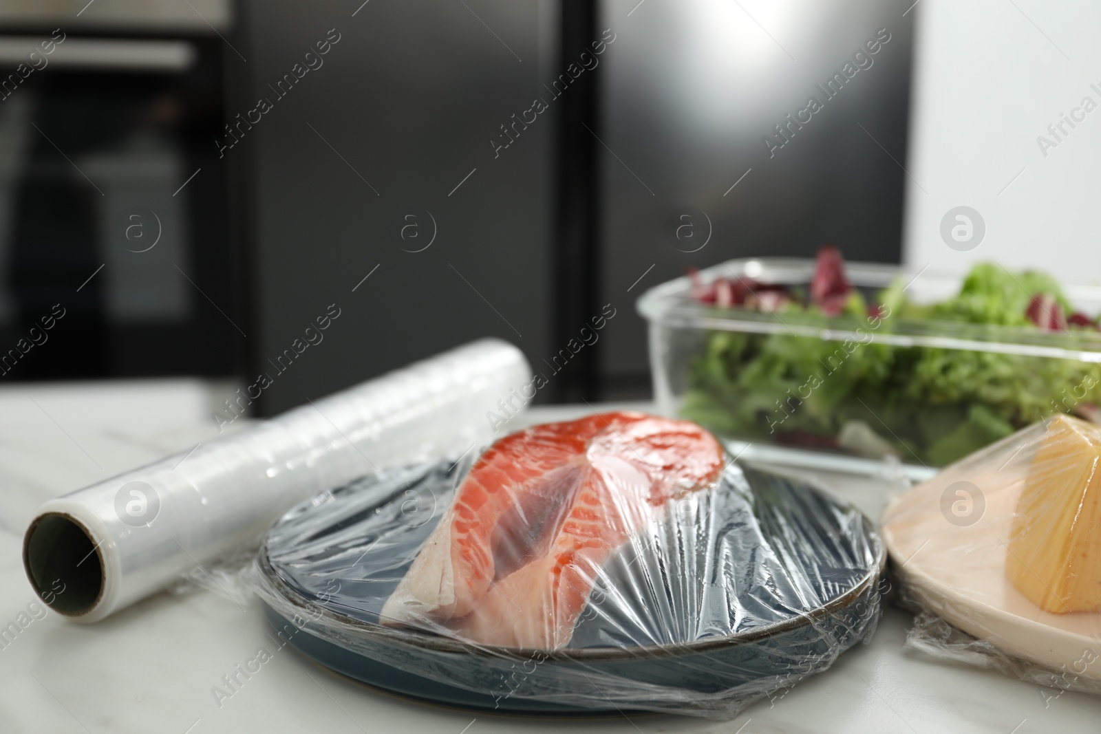 Photo of Plate of salmon with plastic food wrap on white table in kitchen, closeup