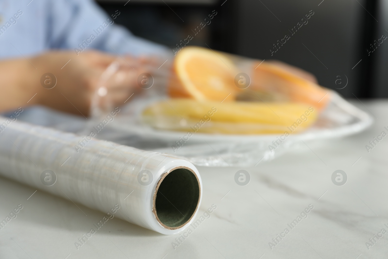 Photo of Woman putting plastic food wrap over plate with fruits at countertop in kitchen, selective focus