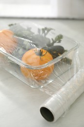 Glass container of fresh vegetables with plastic food wrap on white table, closeup