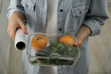 Woman putting plastic food wrap over glass container with vegetables in kitchen, closeup