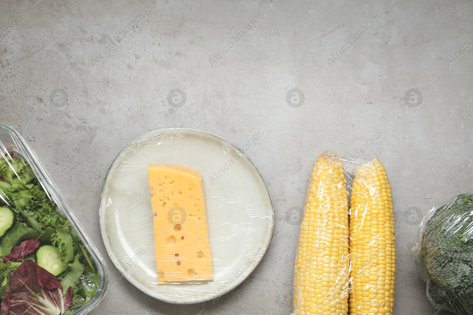 Photo of Different products with plastic food wrap on grey table, flat lay