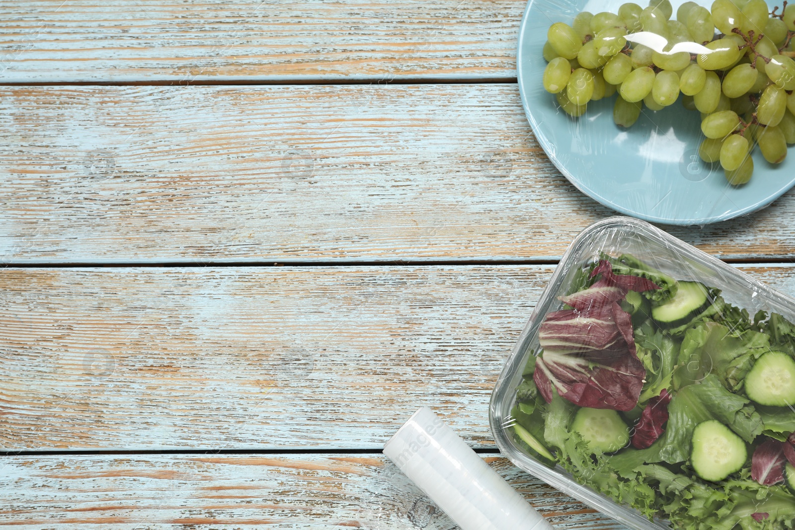 Photo of Different products with plastic food wrap on wooden table, flat lay. Space for text