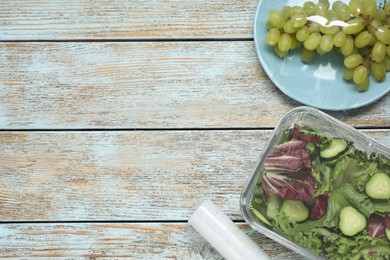 Different products with plastic food wrap on wooden table, flat lay. Space for text