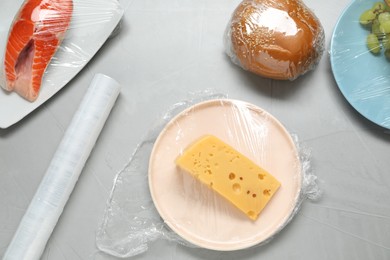 Different products with plastic food wrap on grey table, flat lay