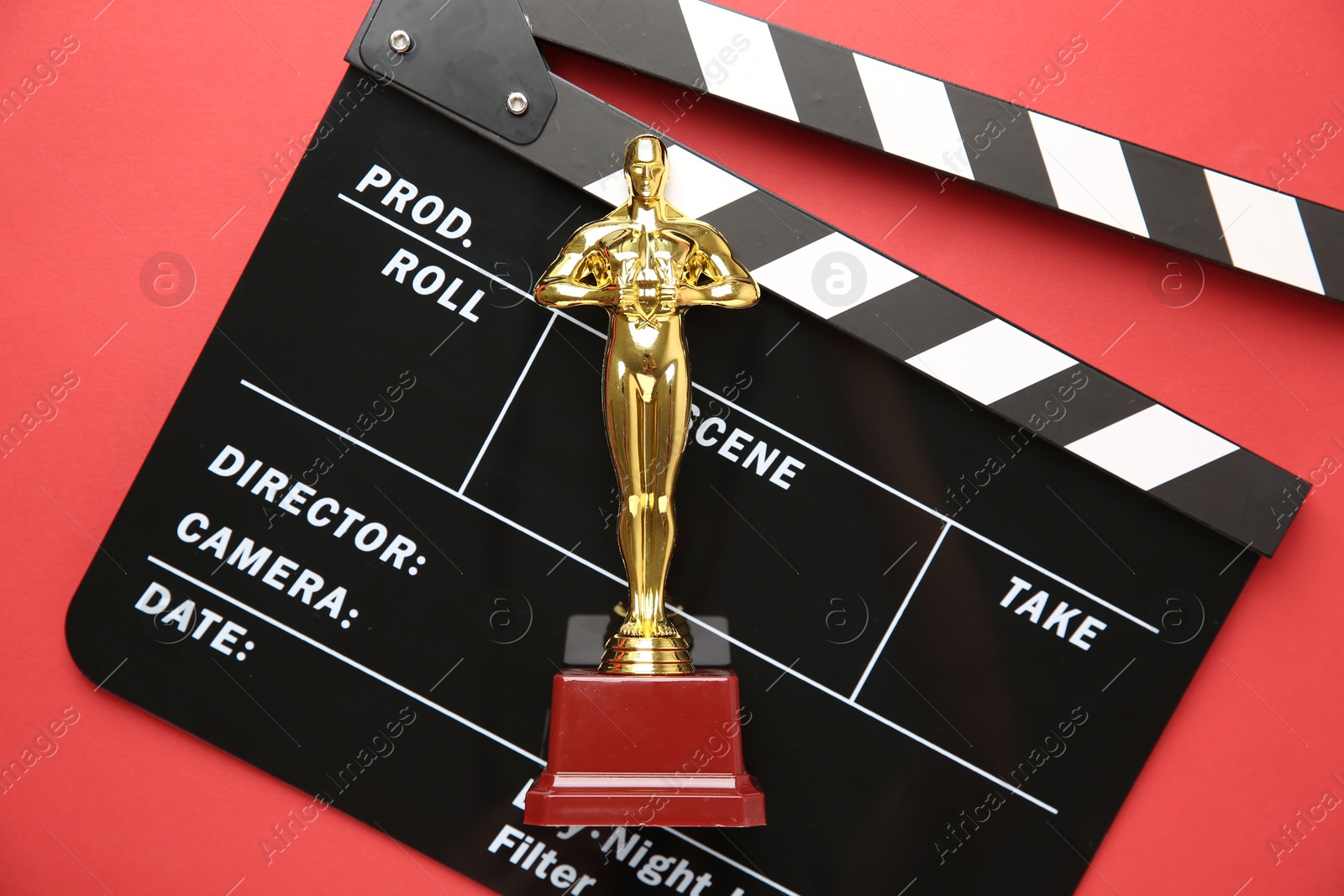 Photo of Golden Oscar award and movie clapper on red background, top view