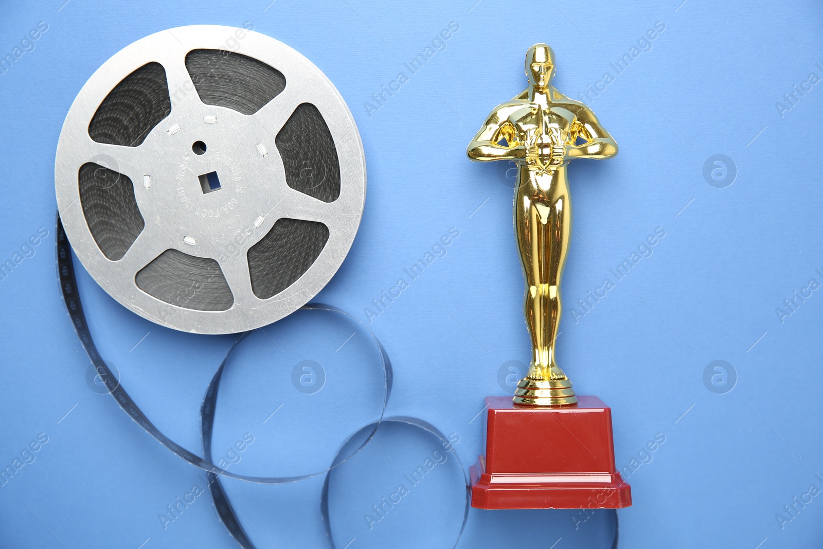 Photo of Golden Oscar award and film reel on light blue background, top view