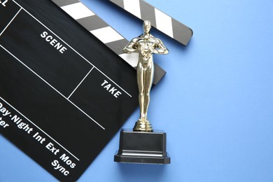 Photo of Golden Oscar award and movie clapper on light blue background, top view