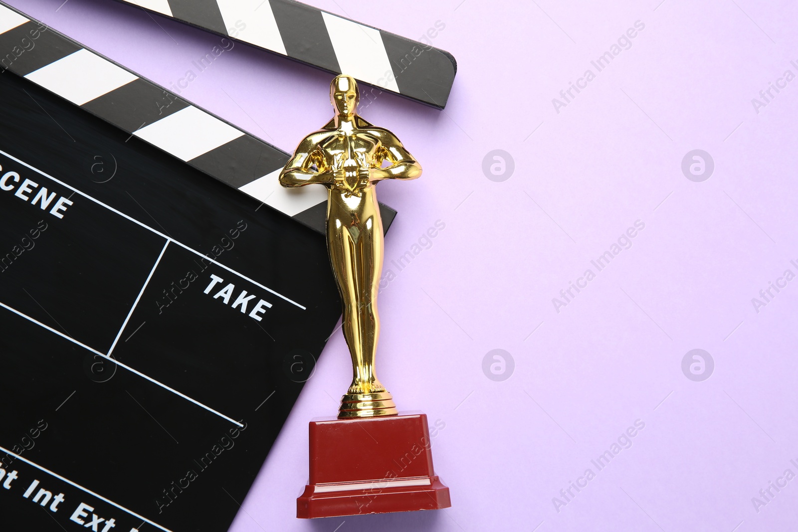 Photo of Golden Oscar award and movie clapper on violet background, top view. Space for text