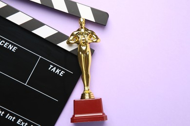 Photo of Golden Oscar award and movie clapper on violet background, top view. Space for text