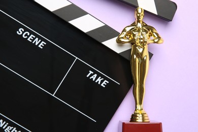 Photo of Golden Oscar award and movie clapper on violet background, top view