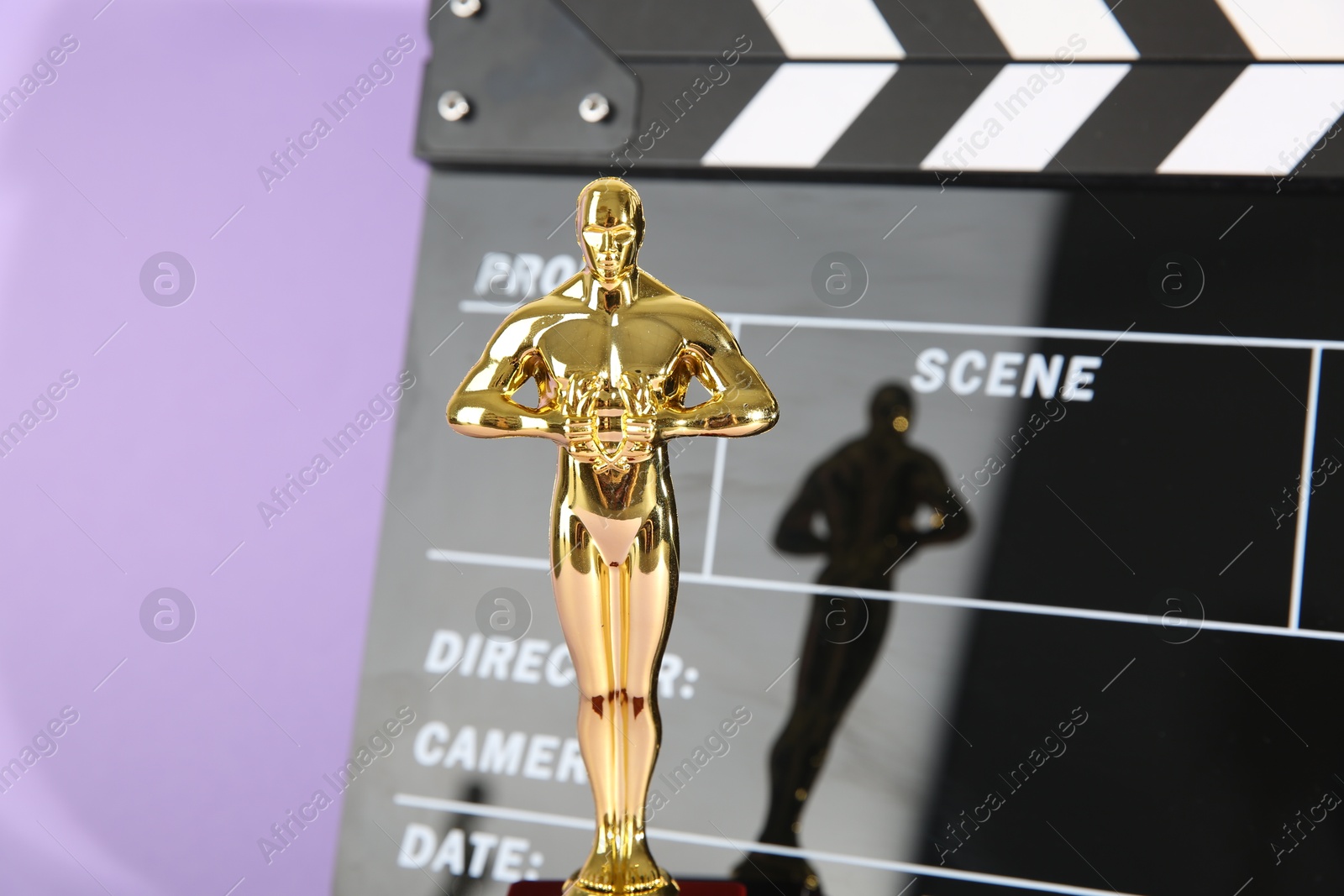 Photo of Golden Oscar award and movie clapper on violet background