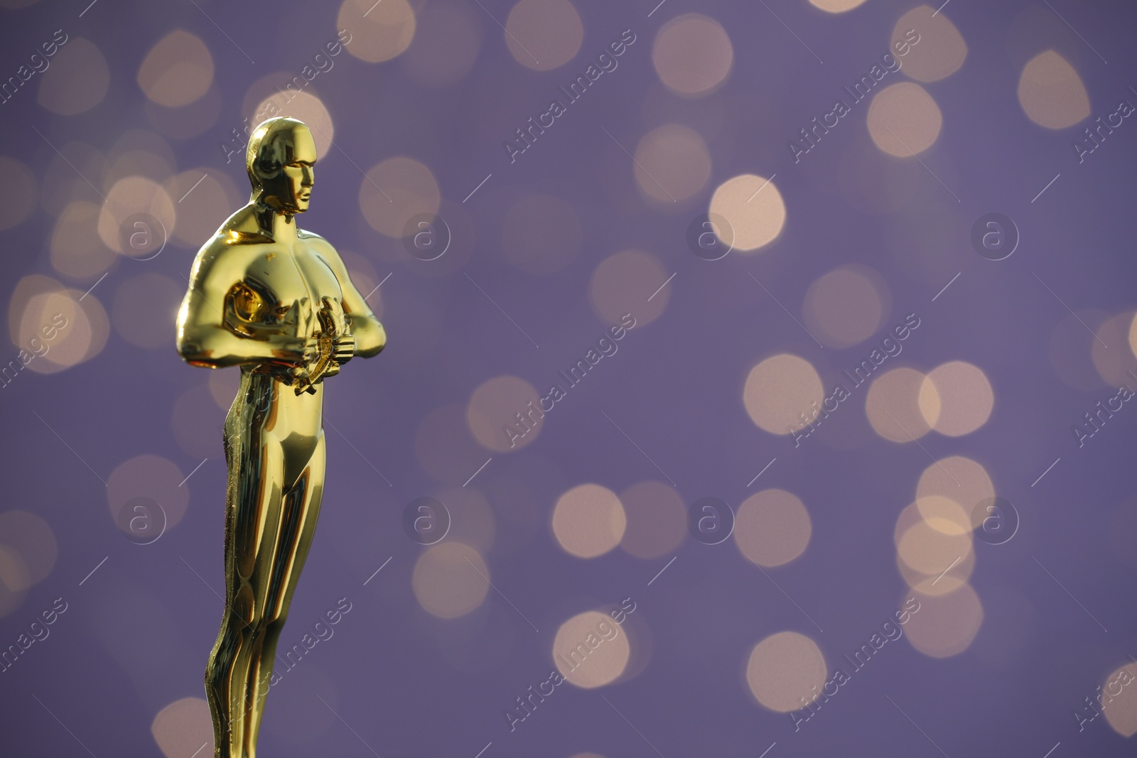 Photo of Golden Oscar award on purple background with blurred lights, space for text