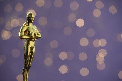 Golden Oscar award on purple background with blurred lights, space for text