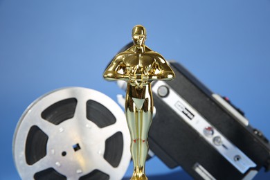 Photo of Golden Oscar award, video camera and film reel on light blue background, selective focus