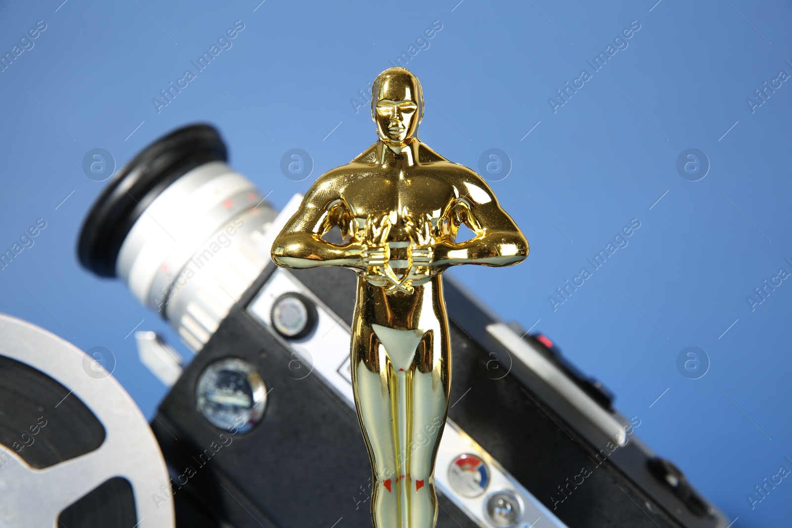 Photo of Golden Oscar award, video camera and film reel on light blue background, closeup