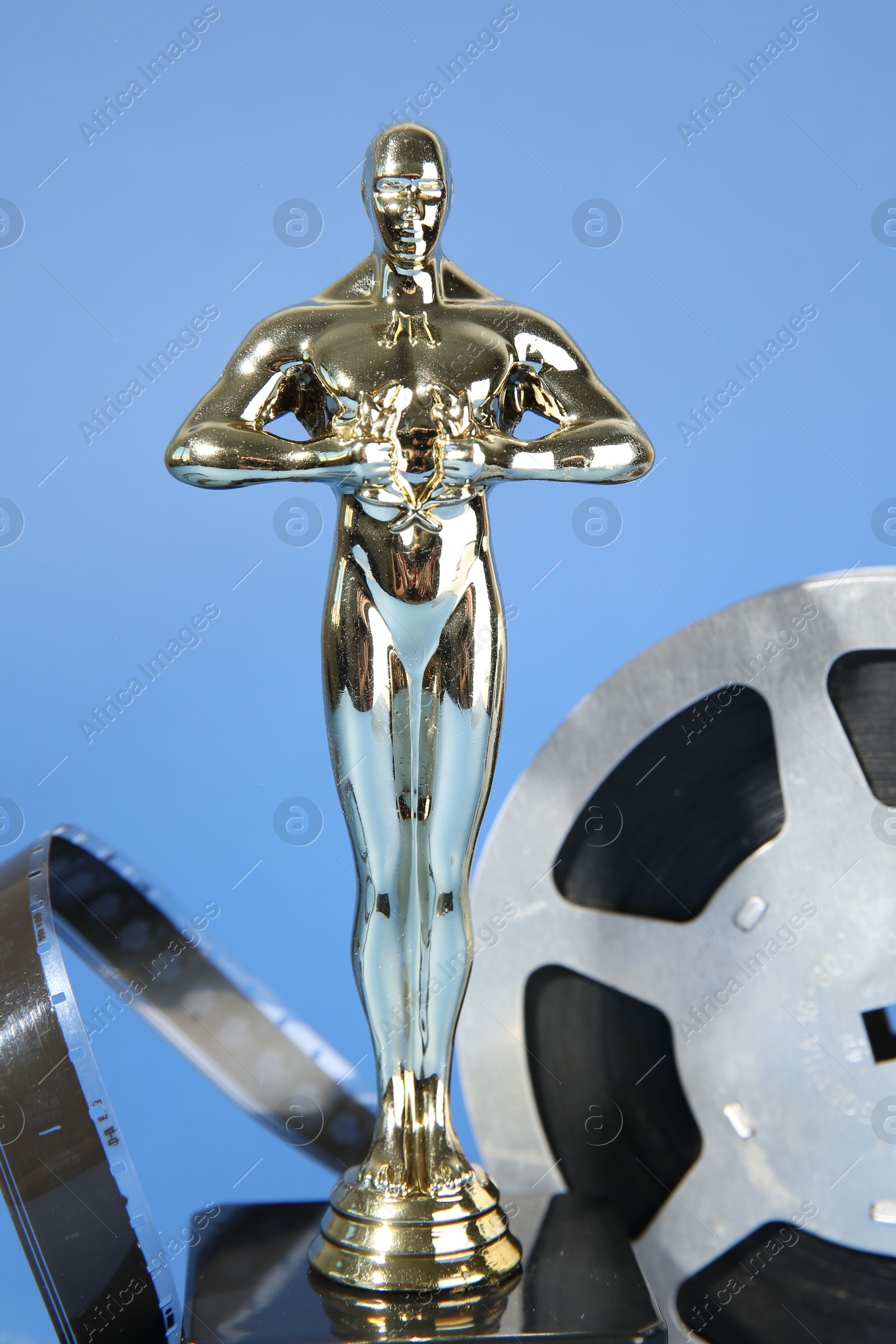 Photo of Golden Oscar award and film reel on light blue background