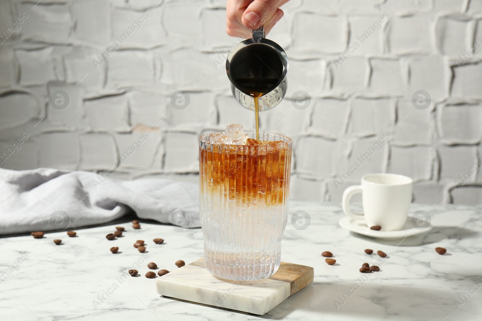 Photo of Woman making refreshing espresso tonic drink at white marble table, closeup