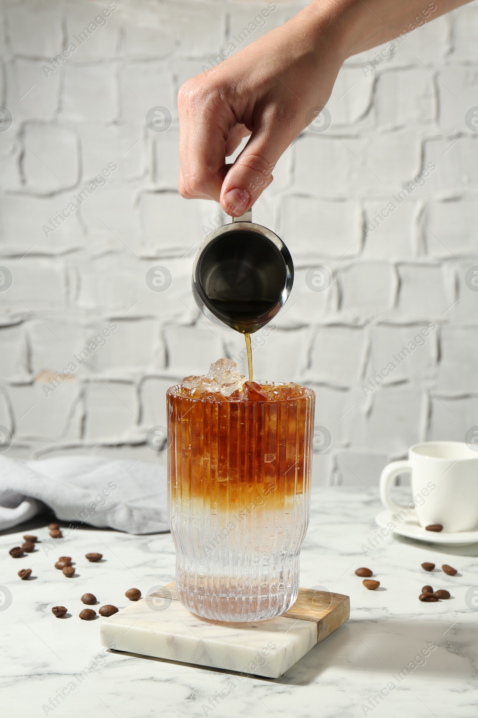 Photo of Woman making refreshing espresso tonic drink at white marble table, closeup