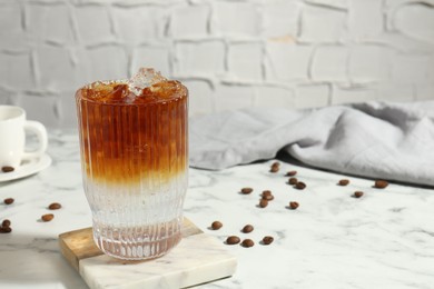 Photo of Refreshing espresso tonic drink and coffee beans on white marble table. Space for text