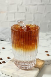 Refreshing espresso tonic drink and coffee beans on white marble table, closeup