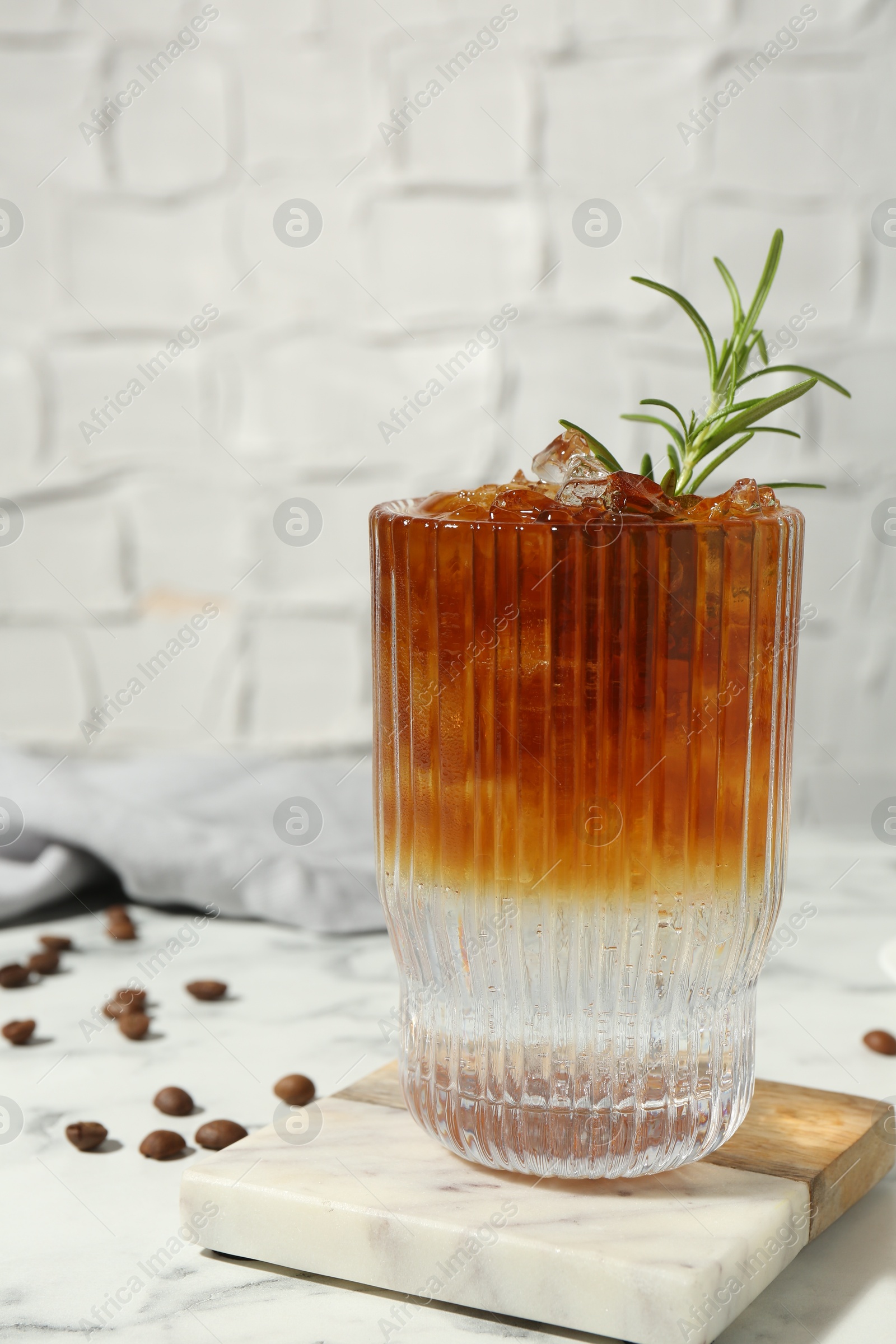 Photo of Refreshing espresso tonic drink with rosemary and coffee beans on white marble table