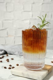 Photo of Refreshing espresso tonic drink with rosemary and coffee beans on white marble table