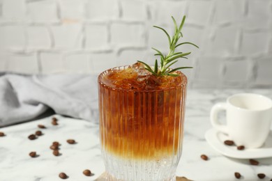 Refreshing espresso tonic drink with rosemary and coffee beans on white marble table, closeup