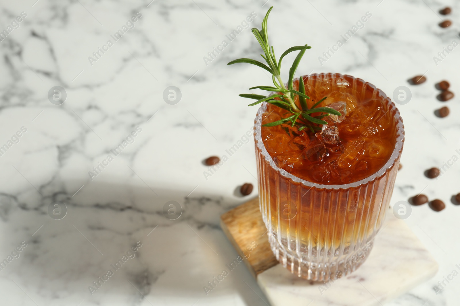 Photo of Refreshing espresso tonic drink with rosemary and coffee beans on white marble table, closeup. Space for text