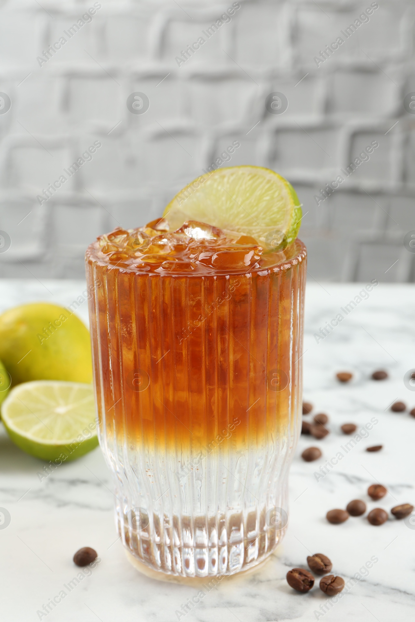 Photo of Refreshing espresso tonic drink with slice of lime and coffee beans on white marble table