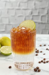 Refreshing espresso tonic drink with slice of lime and coffee beans on white marble table