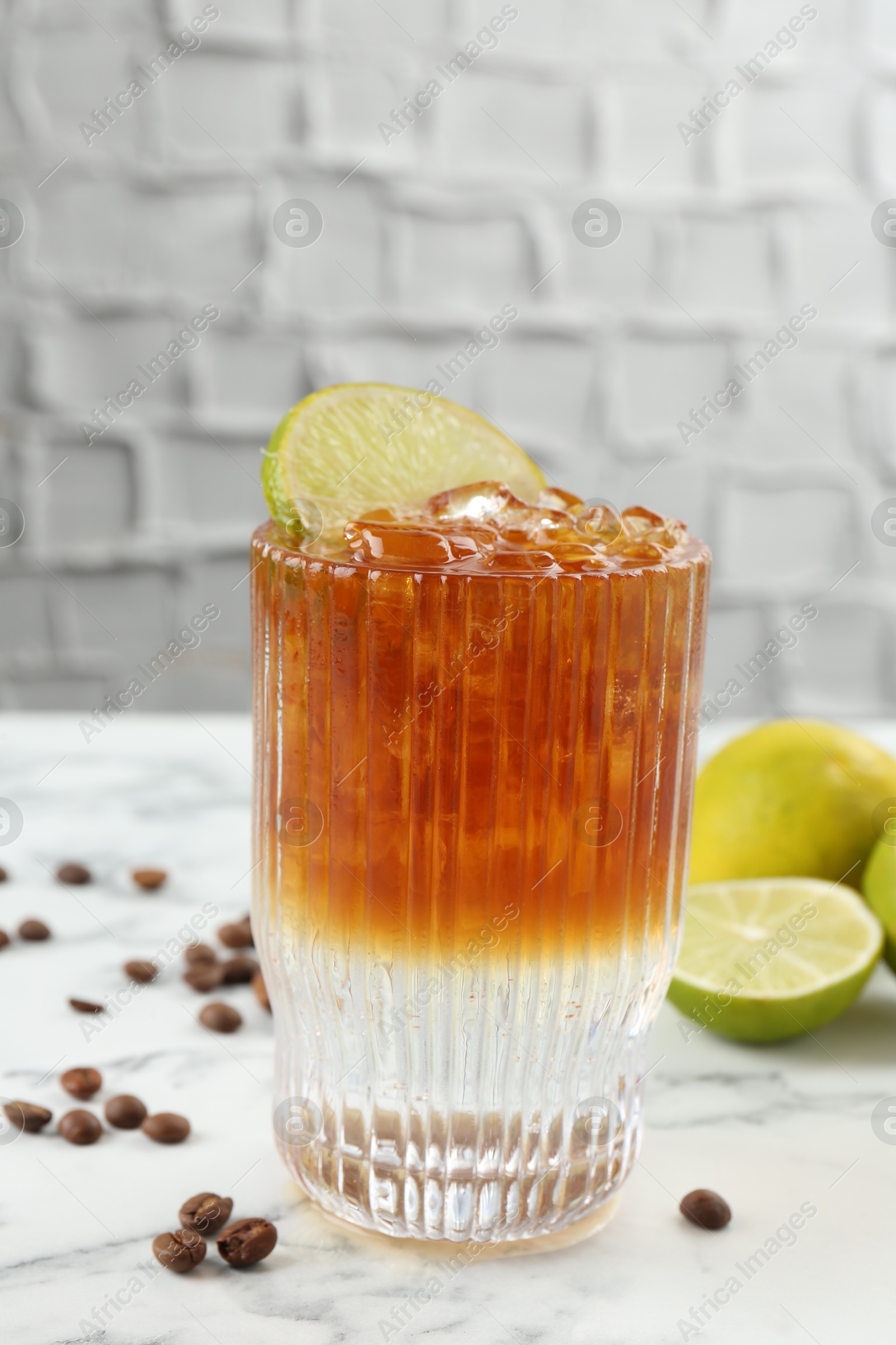 Photo of Refreshing espresso tonic drink with slice of lime and coffee beans on white marble table