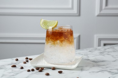 Photo of Refreshing espresso tonic drink with slice of lime and coffee beans on white marble table