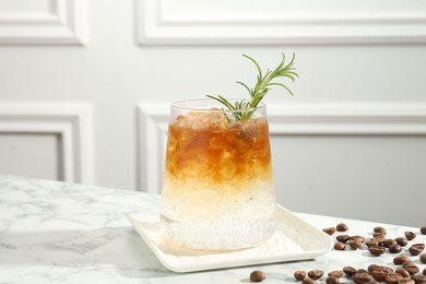 Photo of Refreshing espresso tonic drink with rosemary and coffee beans on white marble table