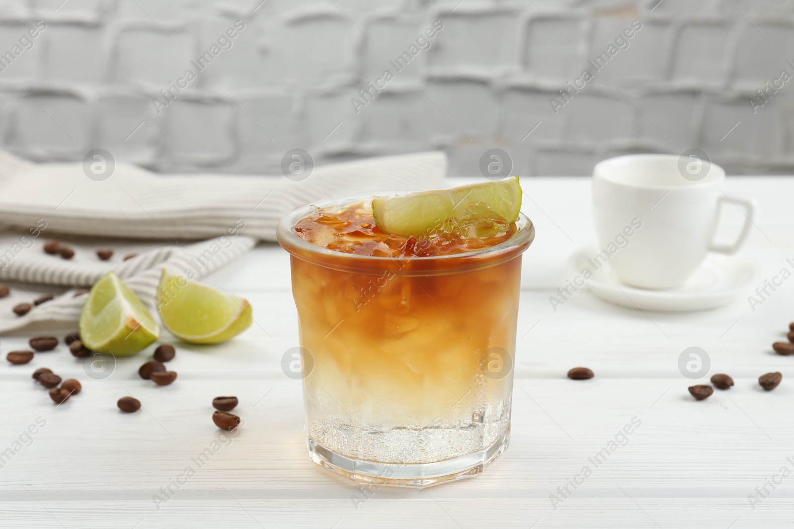 Photo of Refreshing espresso tonic drink with slice of lime and coffee beans on white wooden table