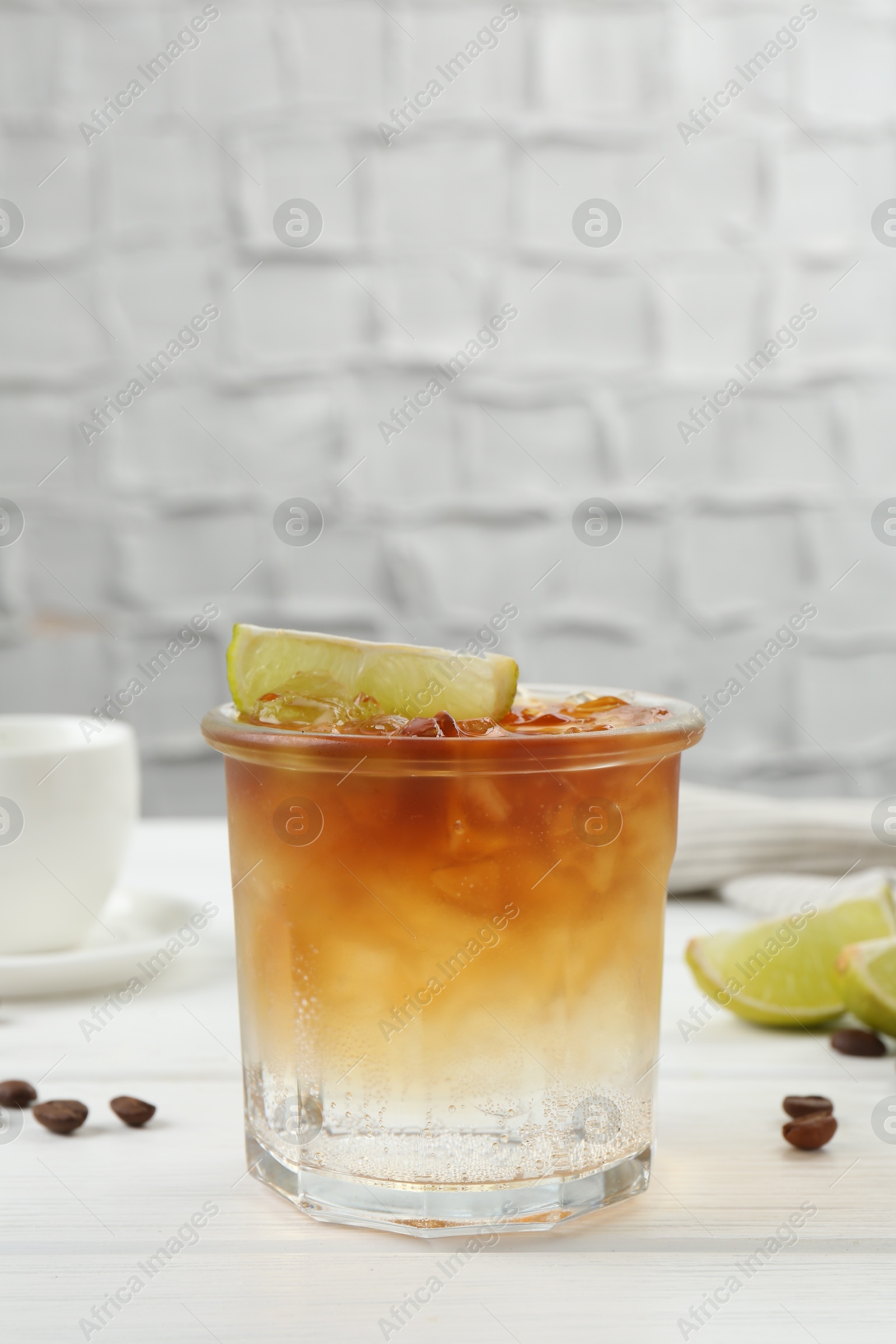 Photo of Refreshing espresso tonic drink with slice of lime and coffee beans on white wooden table