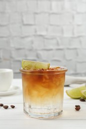 Photo of Refreshing espresso tonic drink with slice of lime and coffee beans on white wooden table