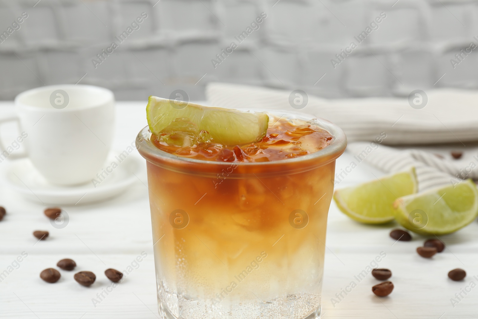 Photo of Refreshing espresso tonic drink with slice of lime and coffee beans on white wooden table, closeup